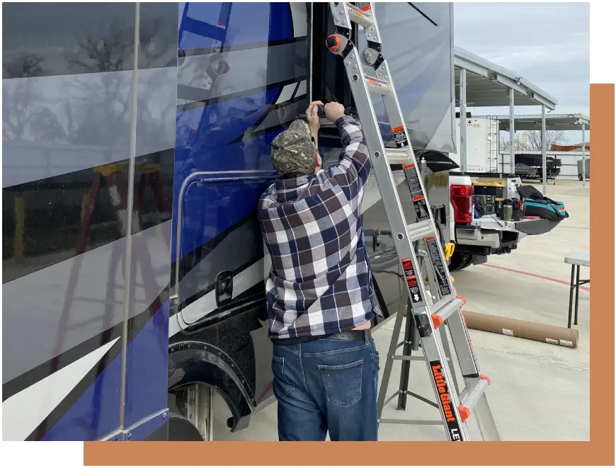 A man on a ladder is working on the side of a bus.